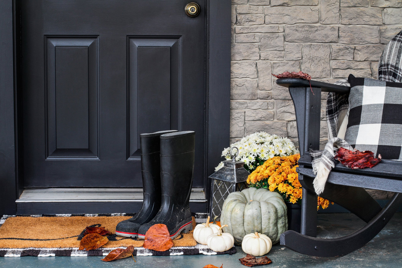Traditional style front porch decorated for autumn with rain boots, heirloom gourds, white pumpkins, mums and rocking chair